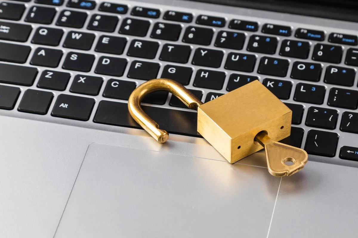 Lucchetto dorato aperto con chiave inserita, appoggiato su una tastiera di computer portatile.