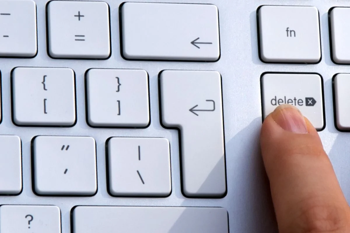 Dito che preme il tasto "delete" su una tastiera bianca di computer.